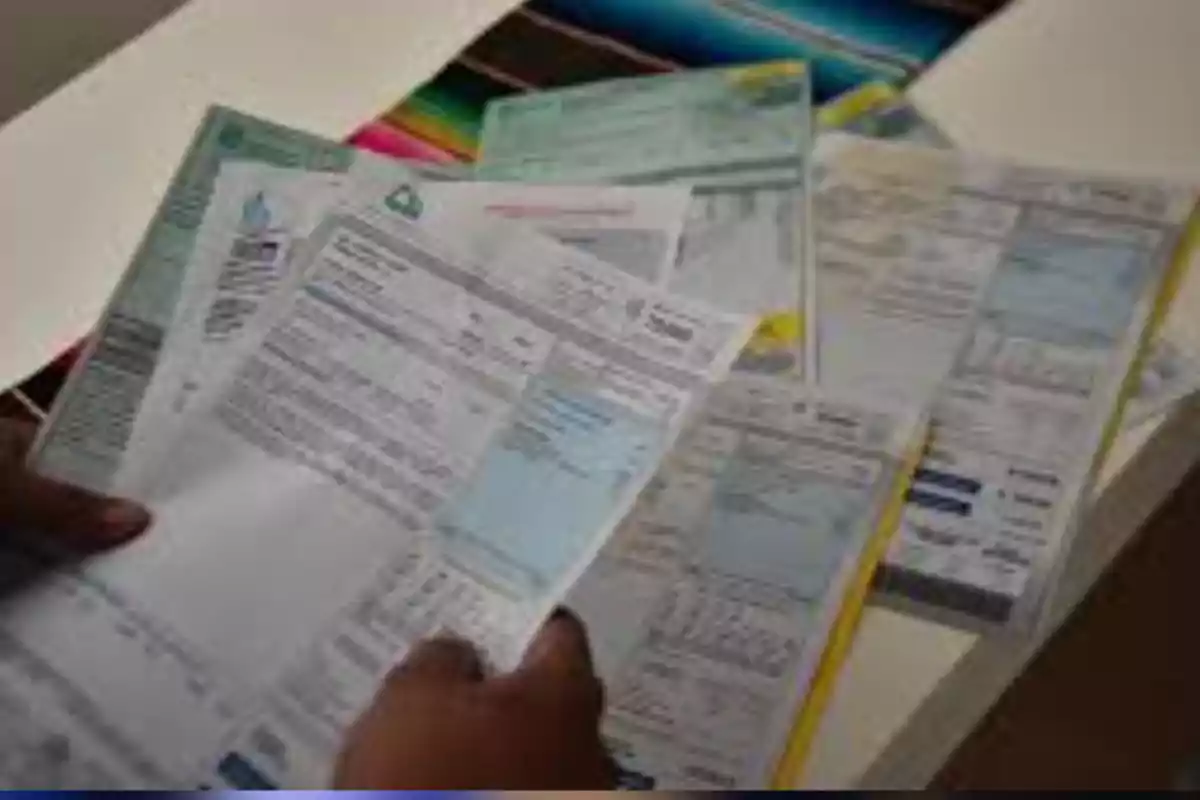 Person holding several utility bills on a table Person holding several utility bills on a table