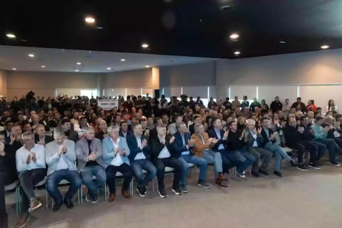 Auditorium full of seated people applauding during an event in a brightly lit hall. Auditorium full of seated people applauding during an event in a brightly lit hall.