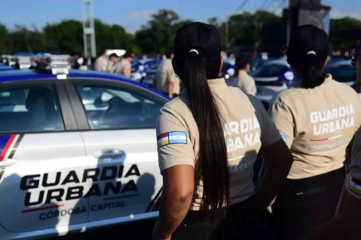 Women from the Córdoba Capital Urban Guard standing with their backs to the camera next to a patrol car during an outdoor event Women from the Córdoba Capital Urban Guard standing with their backs to the camera next to a patrol car during an outdoor event