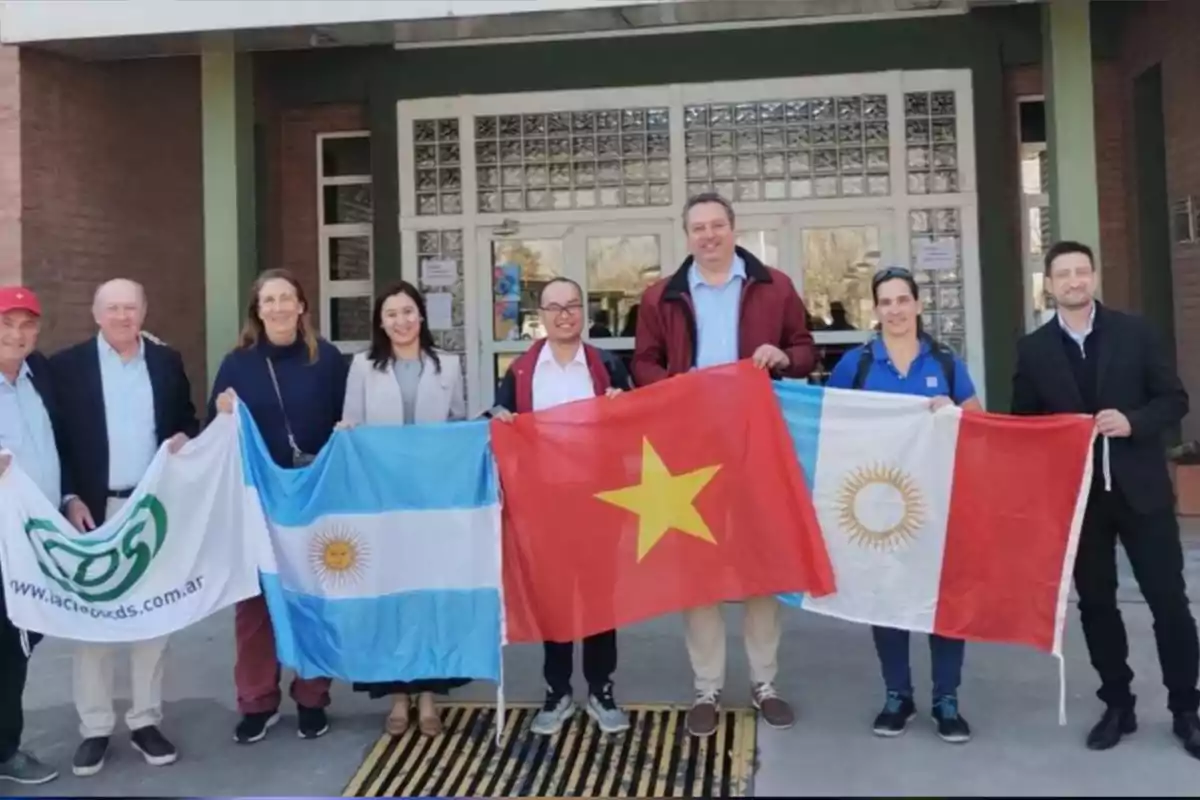 Grupo de personas posando frente a un edificio mientras sostienen banderas de Argentina, Vietnam y una bandera con un logo verde