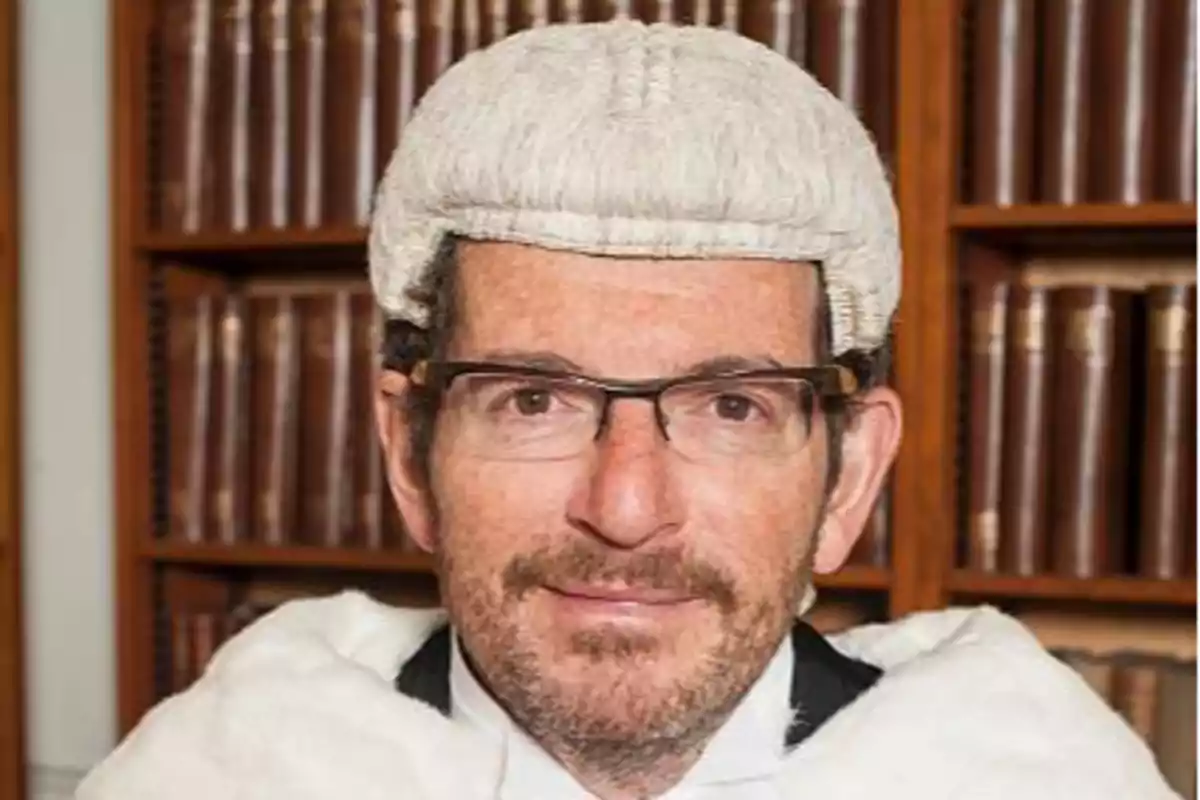 Hombre con gafas y peluca judicial frente a una estantería de libros antiguos Hombre con gafas y peluca judicial frente a una estantería de libros antiguos