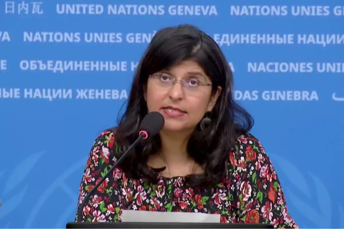 Mujer de cabello oscuro y gafas hablando frente a un micrófono con fondo azul de Naciones Unidas Mujer de cabello oscuro y gafas hablando frente a un micrófono con fondo azul de Naciones Unidas