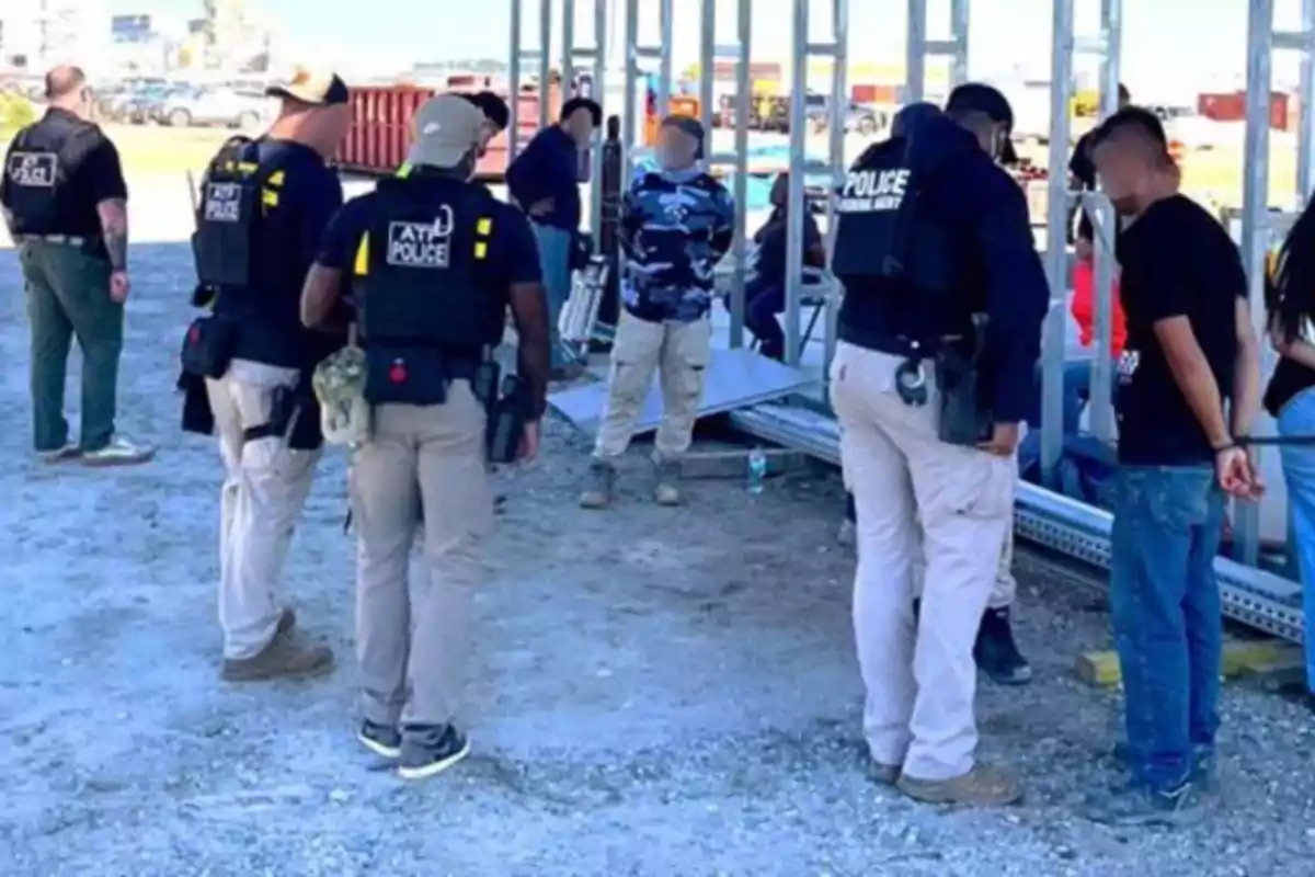 Several police officers detain a group of people in an outdoor construction area.