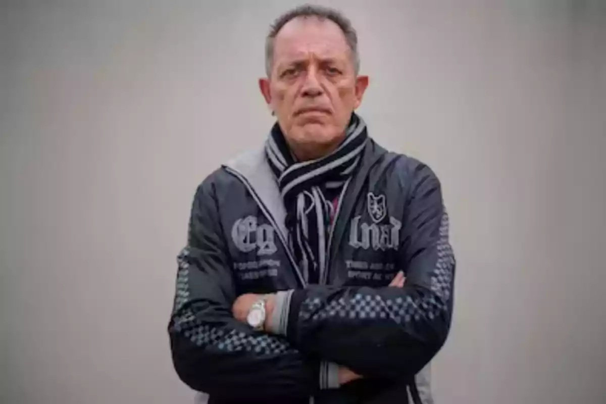 Middle-aged man in a dark jacket and striped scarf posing with his arms crossed in front of a light background Middle-aged man in a dark jacket and striped scarf posing with his arms crossed in front of a light background
