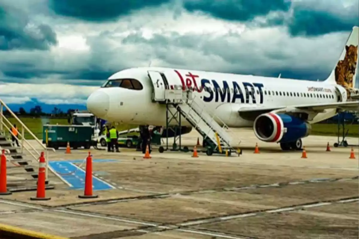 JetSMART airline plane parked on the airport runway with ground staff and boarding stairs under a cloudy sky JetSMART airline plane parked on the airport runway with ground staff and boarding stairs under a cloudy sky