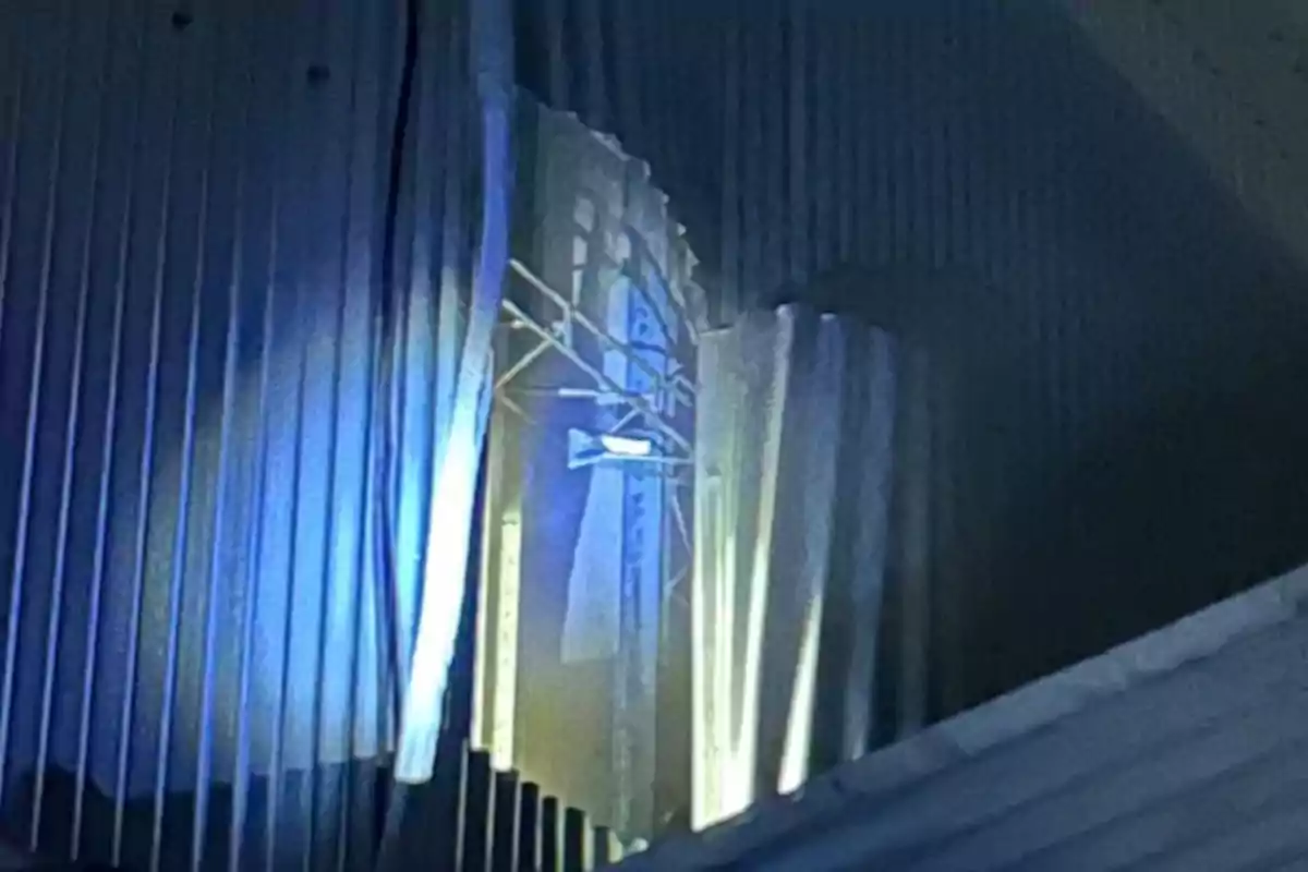 Lámina de metal doblada con luz azul reflejada y estructura metálica visible al fondo Lámina de metal doblada con luz azul reflejada y estructura metálica visible al fondo