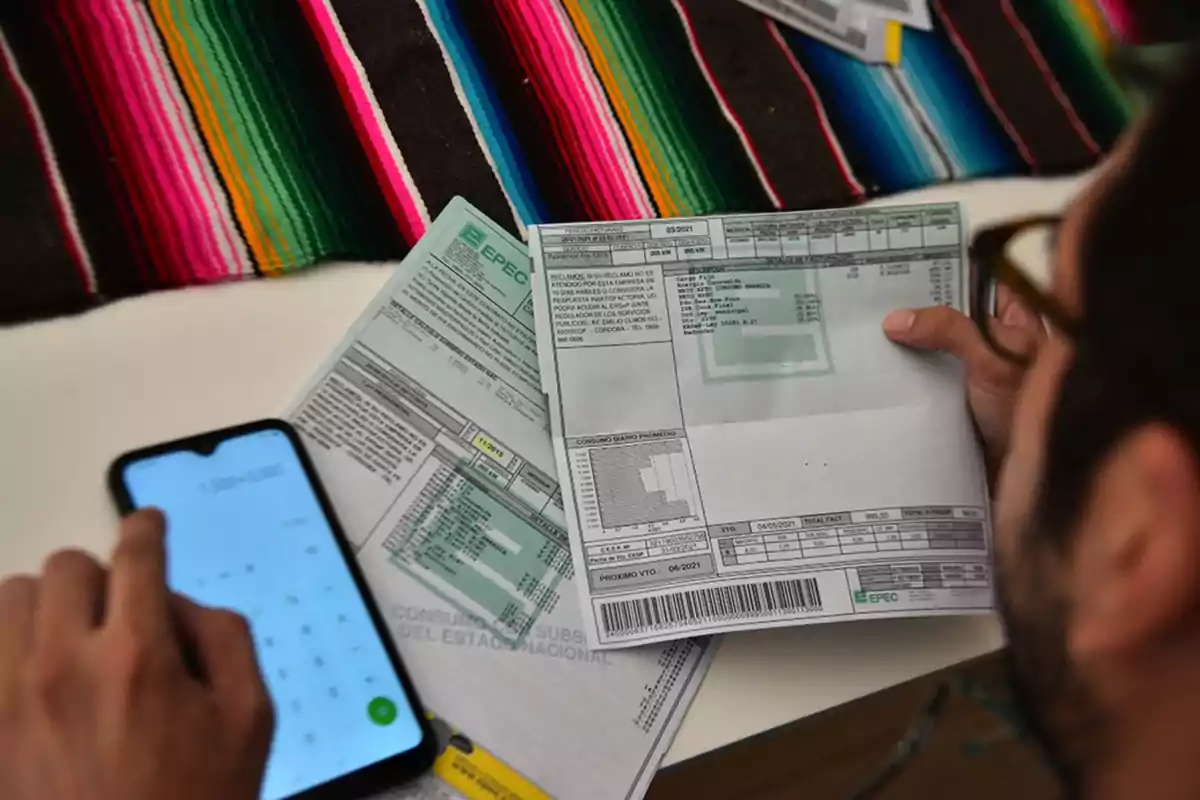 Person reviewing utility bills and using a calculator on their phone at a table with a colorful tablecloth