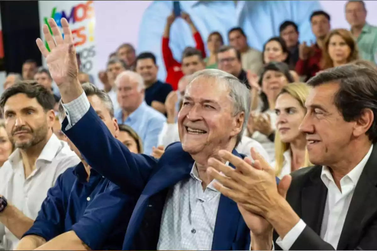 Smiling older man raising his hand at an event surrounded by people applauding Smiling older man raising his hand at an event surrounded by people applauding