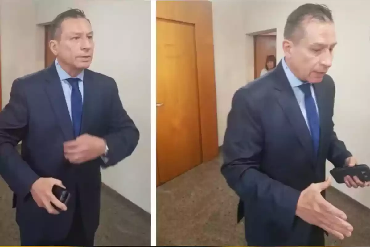 Hombre de traje azul sosteniendo un teléfono móvil en un pasillo con puertas de madera Hombre de traje azul sosteniendo un teléfono móvil en un pasillo con puertas de madera