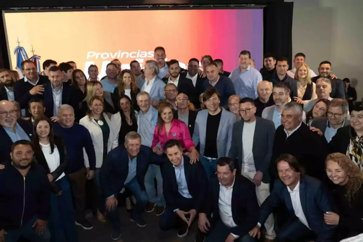 A large group of people posing together and smiling at an event in front of a screen with an orange and purple background
