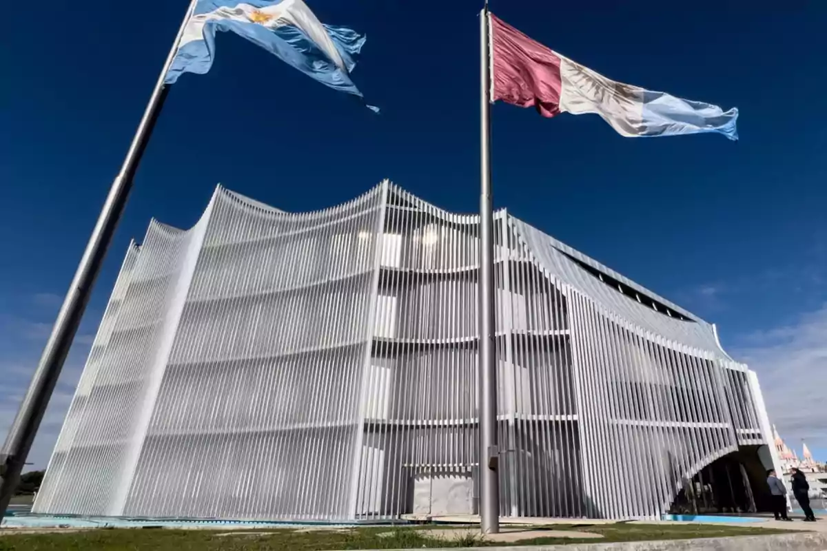 Modern building with a white vertical slat facade and two flags waving in the foreground under a blue sky Modern building with a white vertical slat facade and two flags waving in the foreground under a blue sky