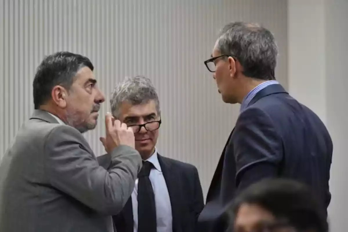 Tres hombres de traje conversan de manera seria en una oficina o sala de reuniones Tres hombres de traje conversan de manera seria en una oficina o sala de reuniones