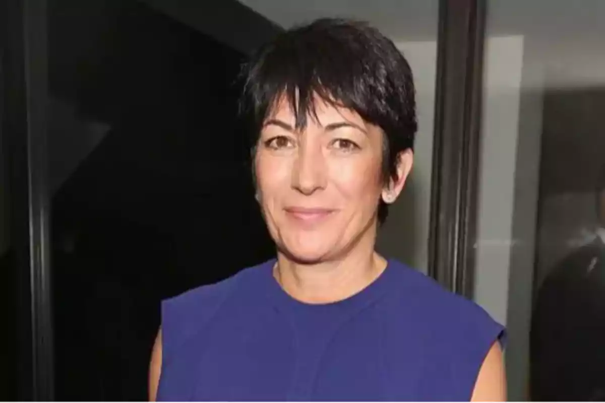 Short-haired dark-haired woman in a blue dress smiling in front of a dark wall Short-haired dark-haired woman in a blue dress smiling in front of a dark wall