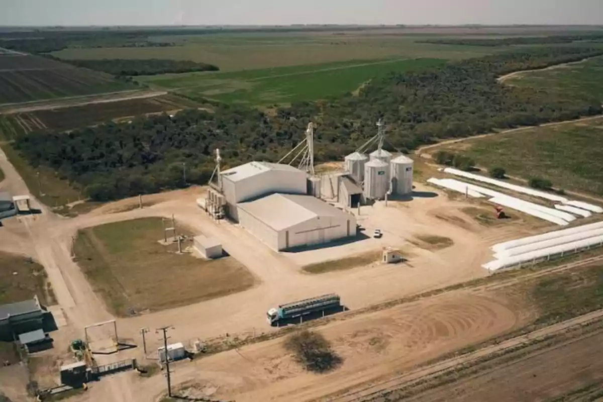 Aerial view of an agricultural facility with metal silos, sheds, and dirt roads surrounded by crop fields and vegetation Aerial view of an agricultural facility with metal silos, sheds, and dirt roads surrounded by crop fields and vegetation