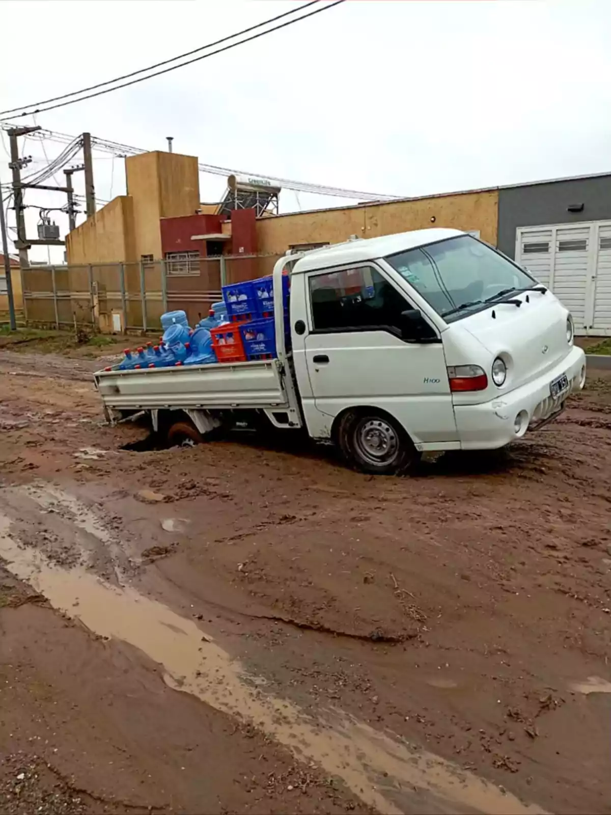 White pickup truck stuck on a muddy dirt road while carrying water jugs and crates of drinks White pickup truck stuck on a muddy dirt road while carrying water jugs and crates of drinks