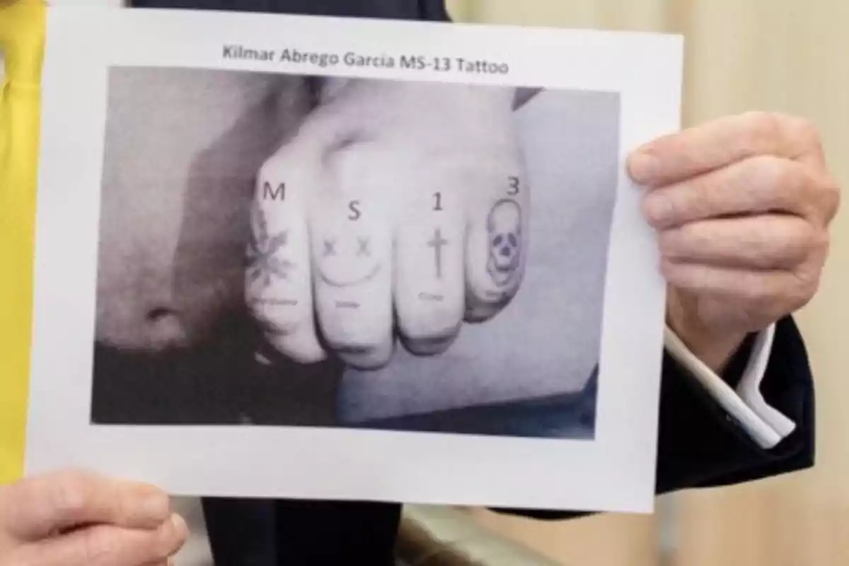 Persona sosteniendo una hoja con una fotografía en blanco y negro de una mano tatuada con símbolos y letras en los nudillos