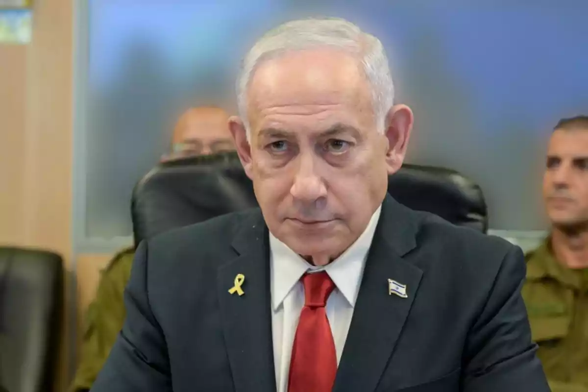 Gray-haired man in a dark suit and red tie sitting in a room next to people in military uniforms Gray-haired man in a dark suit and red tie sitting in a room next to people in military uniforms