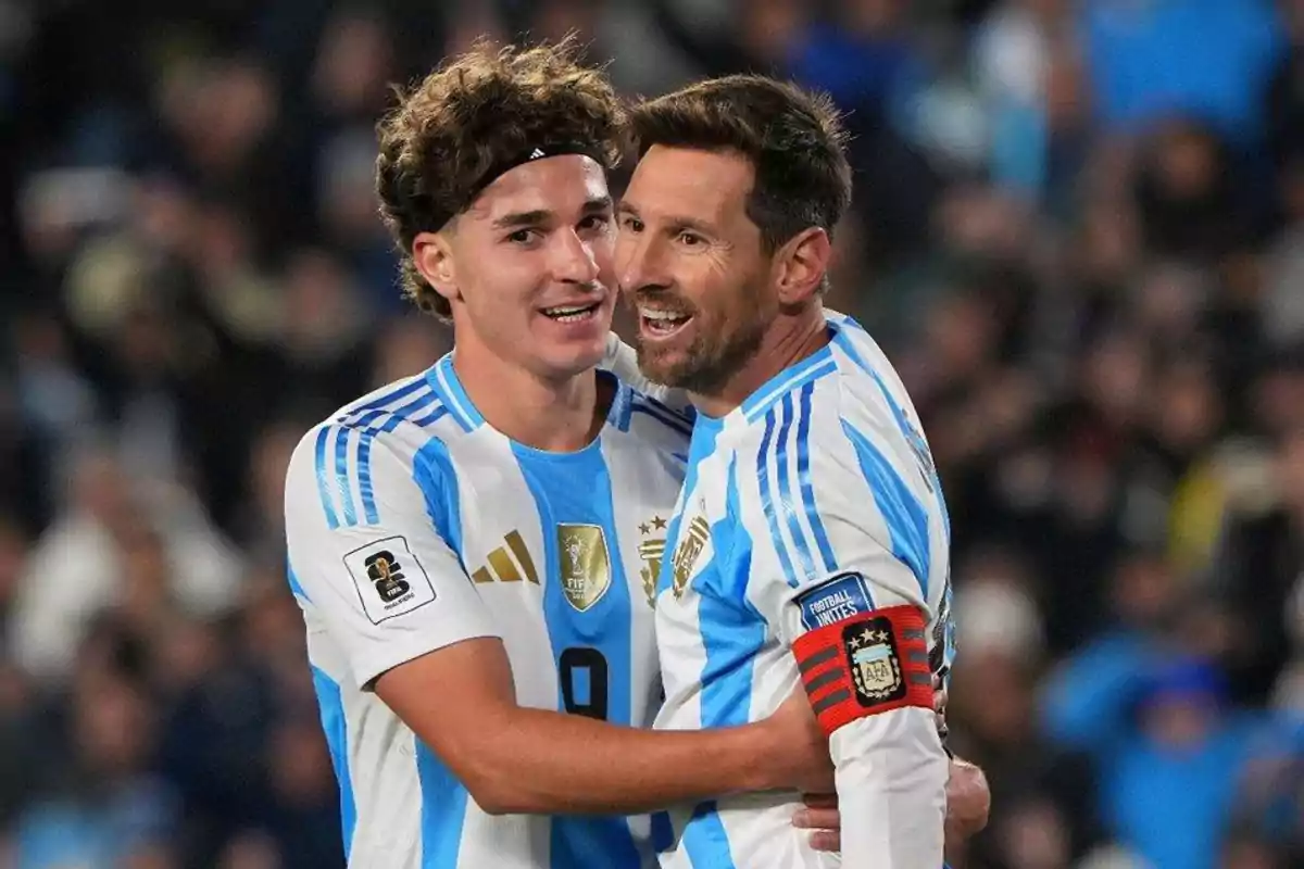 Dos futbolistas de la selección argentina celebran abrazados en el campo durante un partido