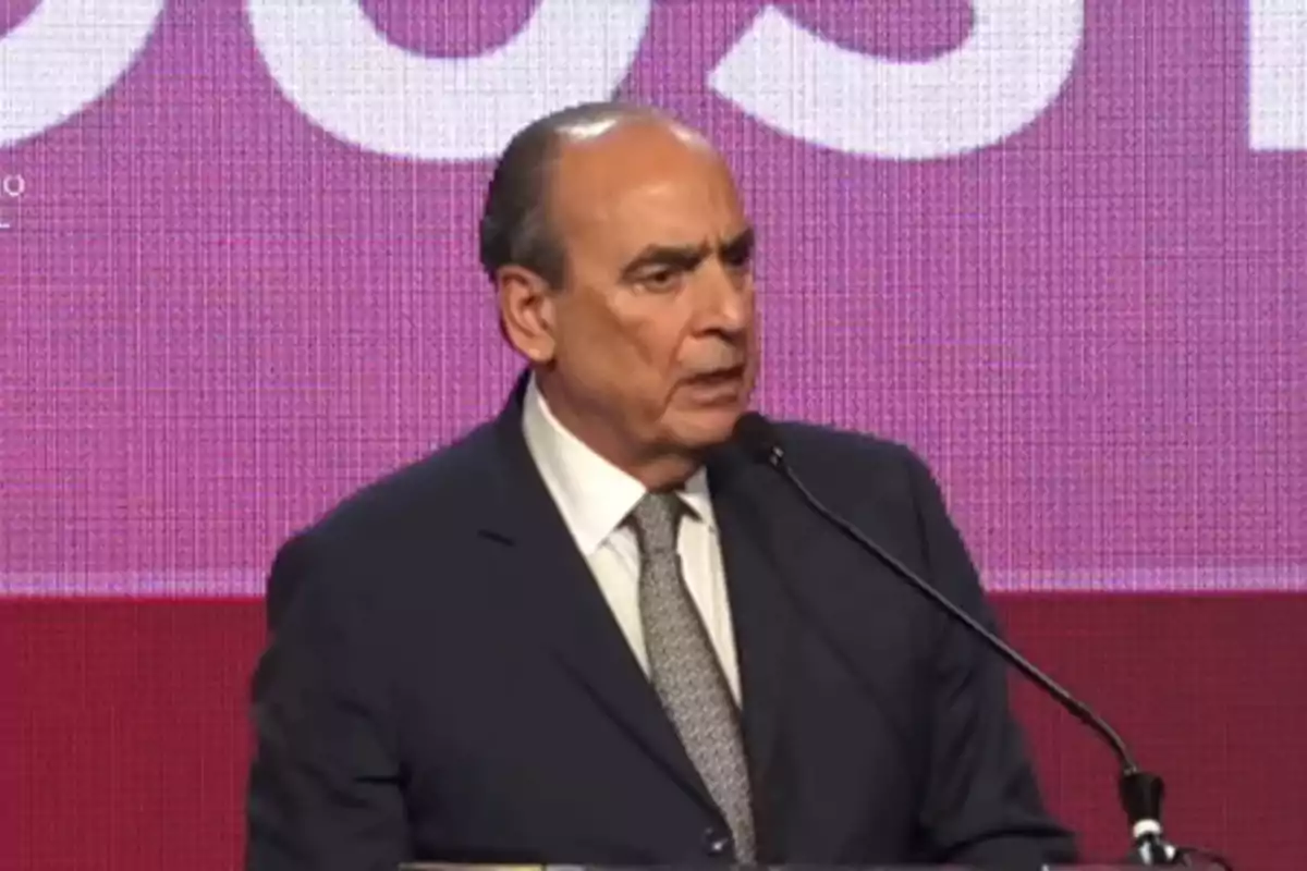 Man in a suit speaking in front of a microphone with a pink background Man in a suit speaking in front of a microphone with a pink background