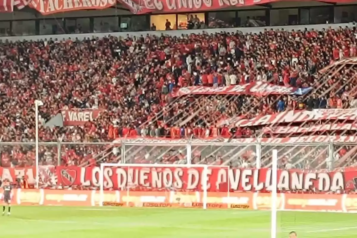 Tribuna llena de hinchas vestidos de rojo en un estadio de fútbol con banderas y carteles alentando a su equipo