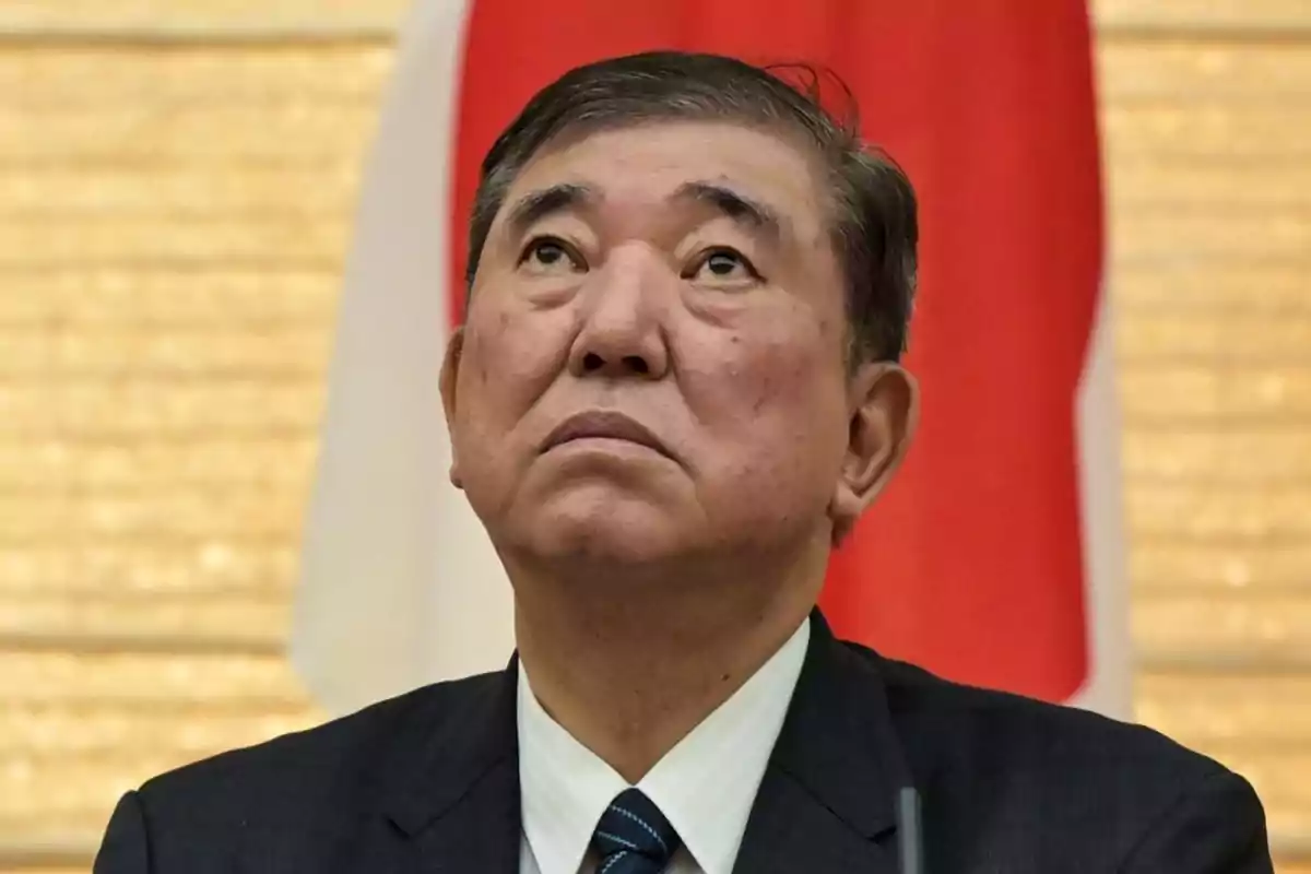 Man in a dark suit looking up with a serious expression and a red and white flag background Man in a dark suit looking up with a serious expression and a red and white flag background
