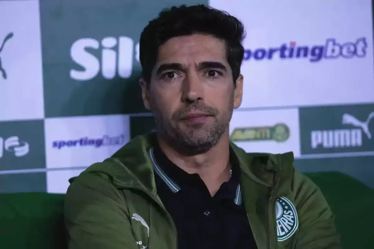 Man wearing a green Palmeiras club jacket sitting in front of a background with sponsor logos Man wearing a green Palmeiras club jacket sitting in front of a background with sponsor logos