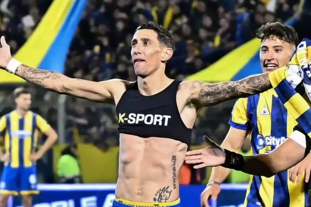 Soccer player celebrating with arms wide open in a stadium full of fans while another player in a yellow and blue uniform approaches smiling Soccer player celebrating with arms wide open in a stadium full of fans while another player in a yellow and blue uniform approaches smiling