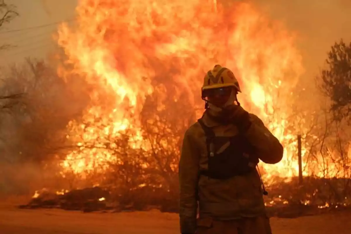 Firefighter with protective gear standing in front of a large wildfire Firefighter with protective gear standing in front of a large wildfire