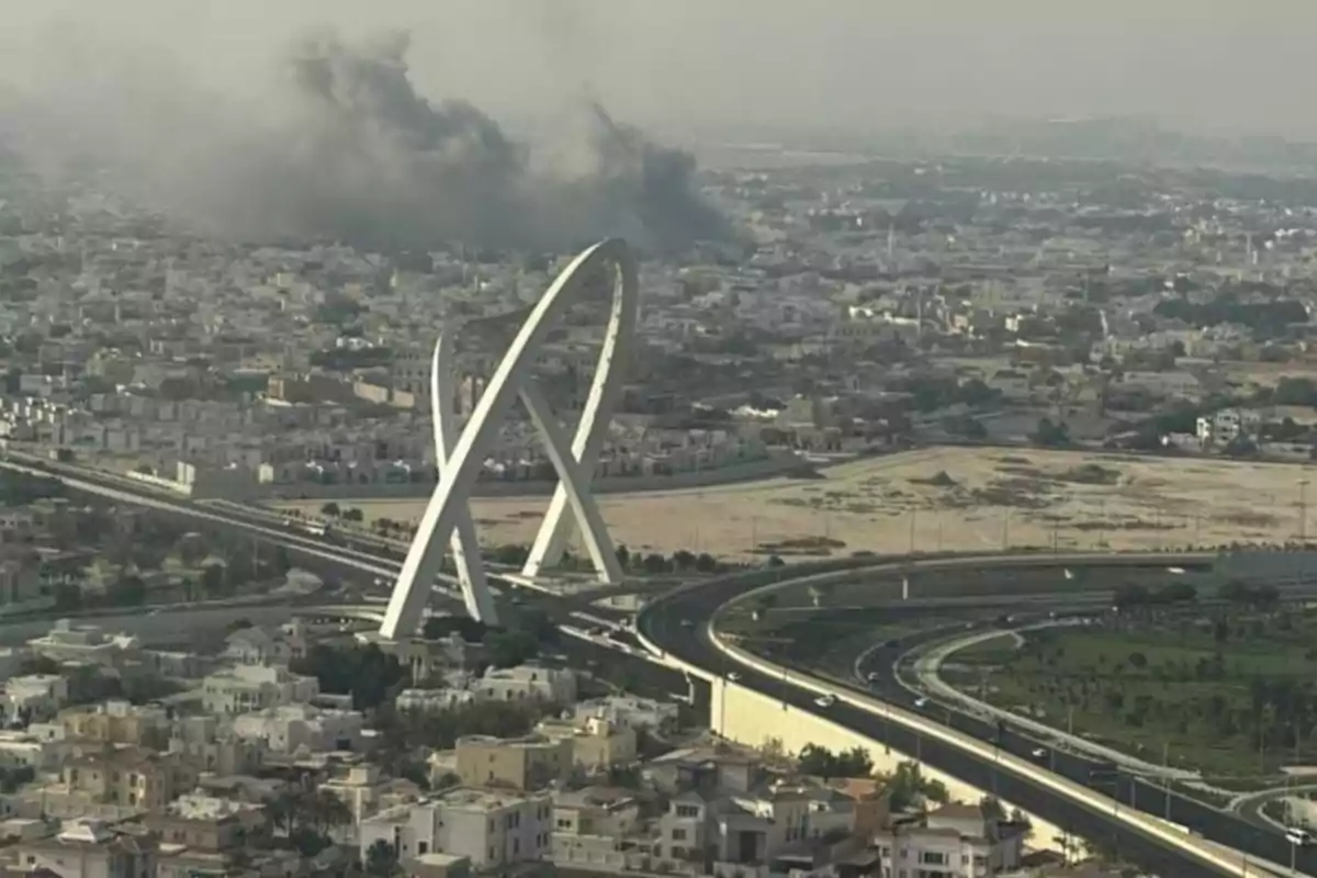 Vista aérea de una ciudad con un puente moderno en primer plano y una columna de humo negro al fondo Vista aérea de una ciudad con un puente moderno en primer plano y una columna de humo negro al fondo
