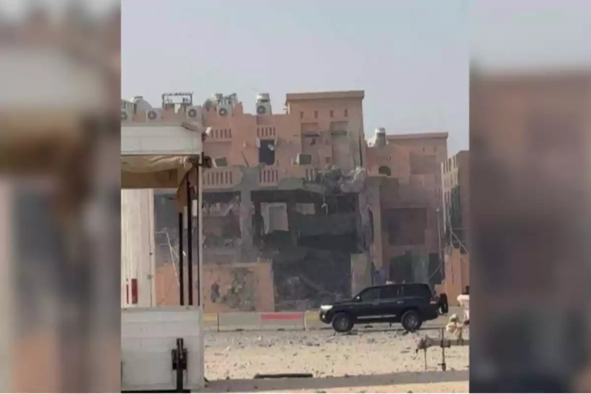 Edificio de color marrón parcialmente destruido con un vehículo negro estacionado al frente y escombros en el suelo Edificio de color marrón parcialmente destruido con un vehículo negro estacionado al frente y escombros en el suelo