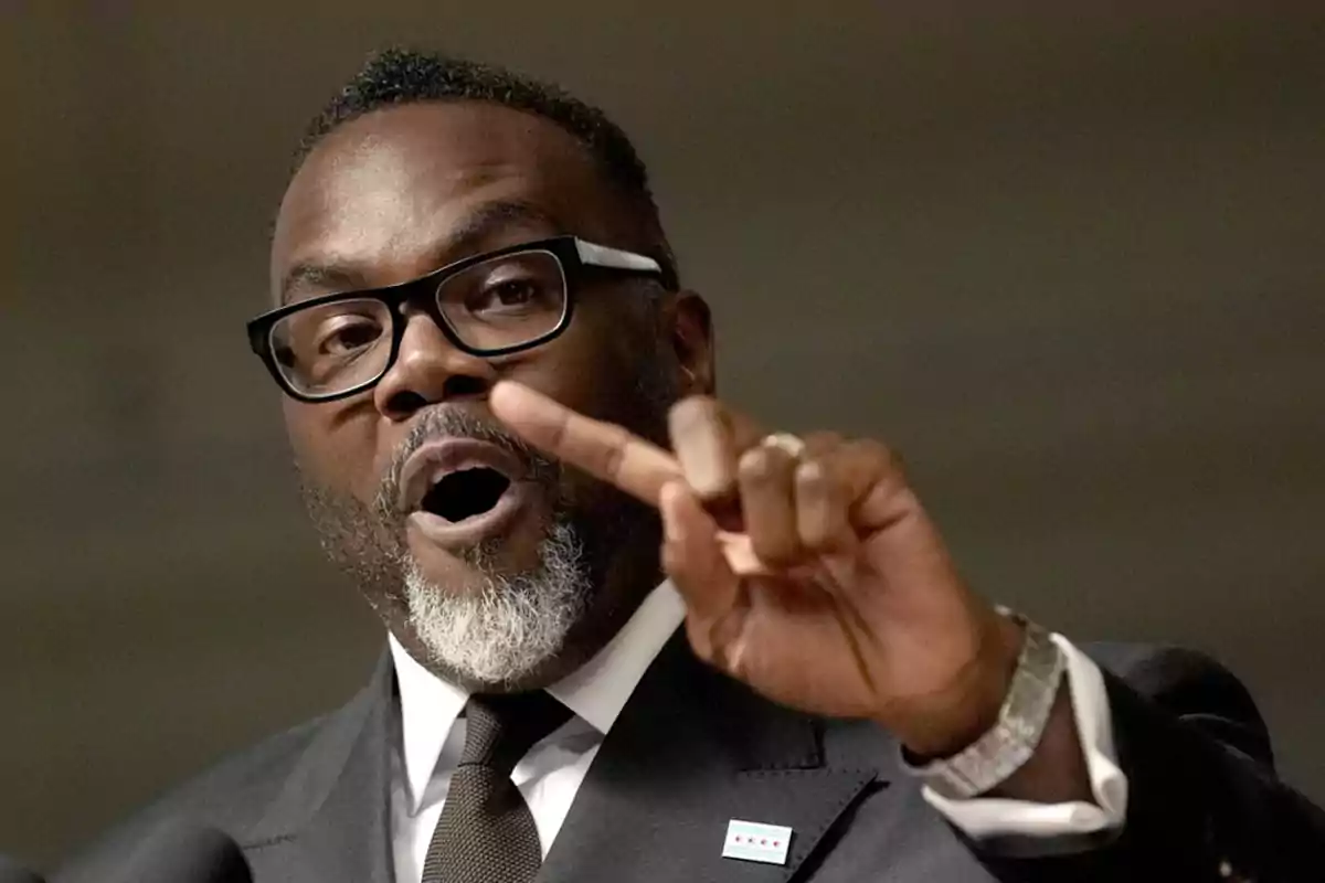 Man with glasses and a graying beard speaking and raising two fingers while wearing a dark suit and tie Man with glasses and a graying beard speaking and raising two fingers while wearing a dark suit and tie