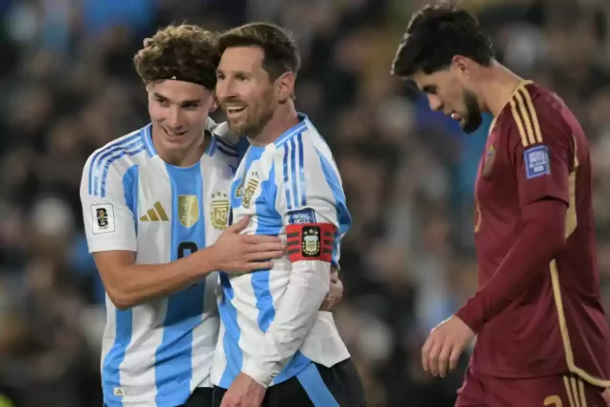Two players from the Argentine national soccer team celebrate hugging while a player from the opposing team walks with his head down. Two players from the Argentine national soccer team celebrate hugging while a player from the opposing team walks with his head down.
