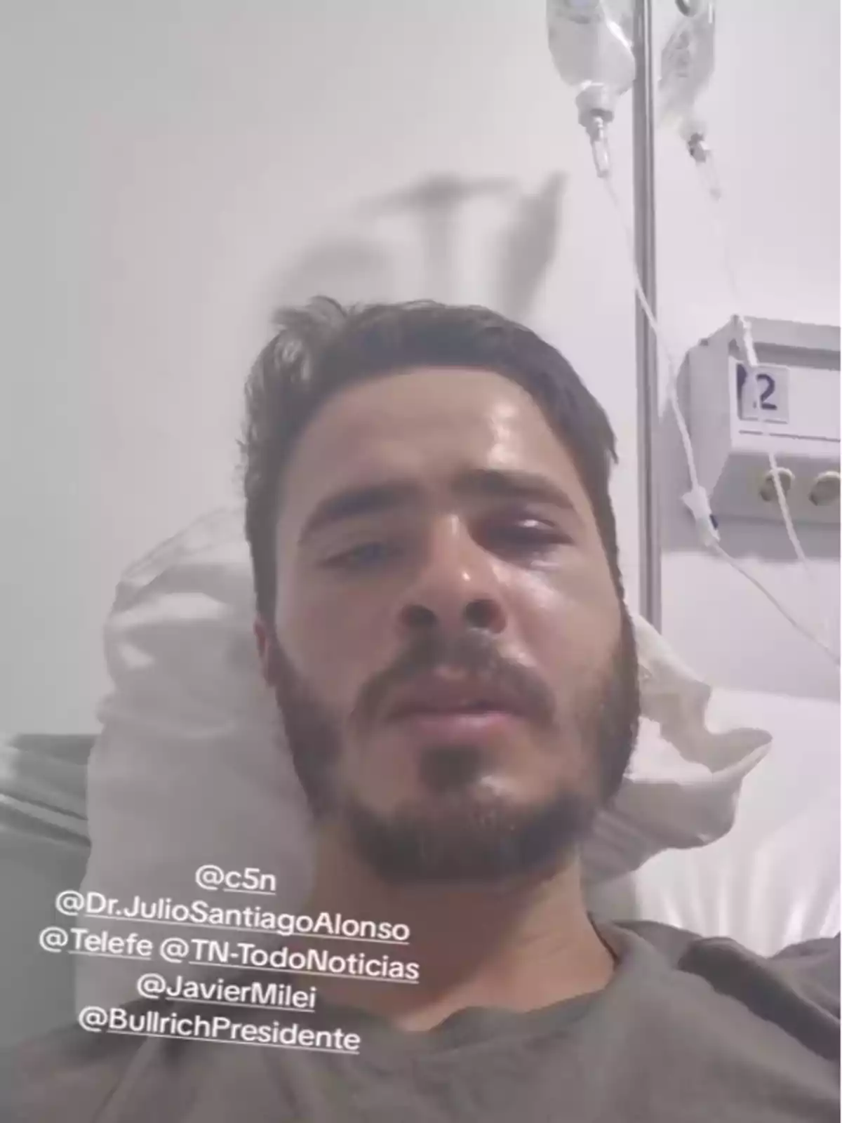 Hombre joven con barba recostado en una cama de hospital con suero conectado y varias menciones de cuentas en redes sociales sobre la imagen Hombre joven con barba recostado en una cama de hospital con suero conectado y varias menciones de cuentas en redes sociales sobre la imagen