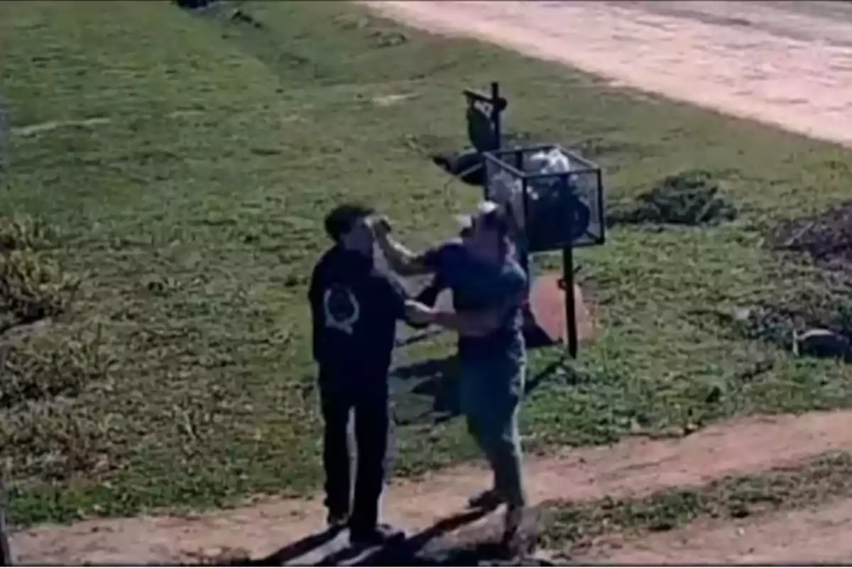 Dos personas discuten y una de ellas empuja a la otra en un camino de tierra junto a un basurero en un área verde