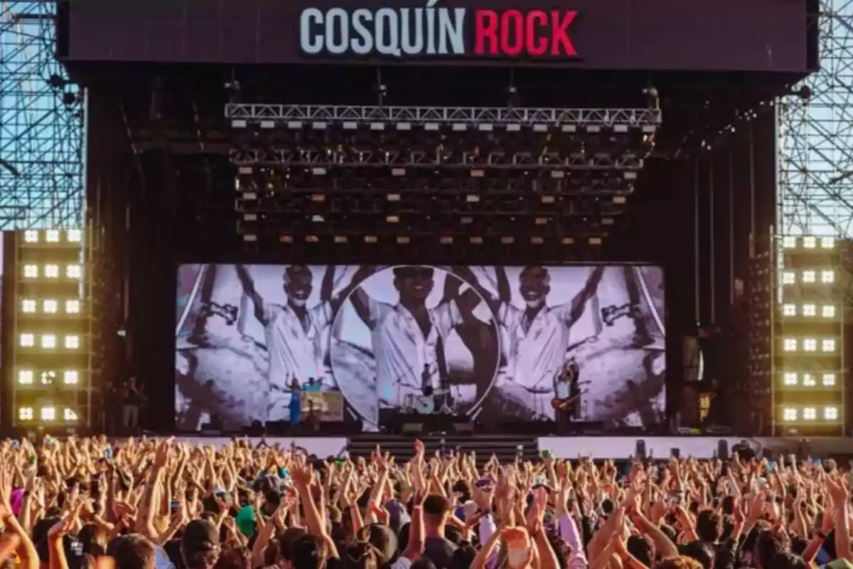 Escenario principal del festival Cosquín Rock con una multitud de personas levantando las manos y una pantalla gigante mostrando imágenes en blanco y negro.