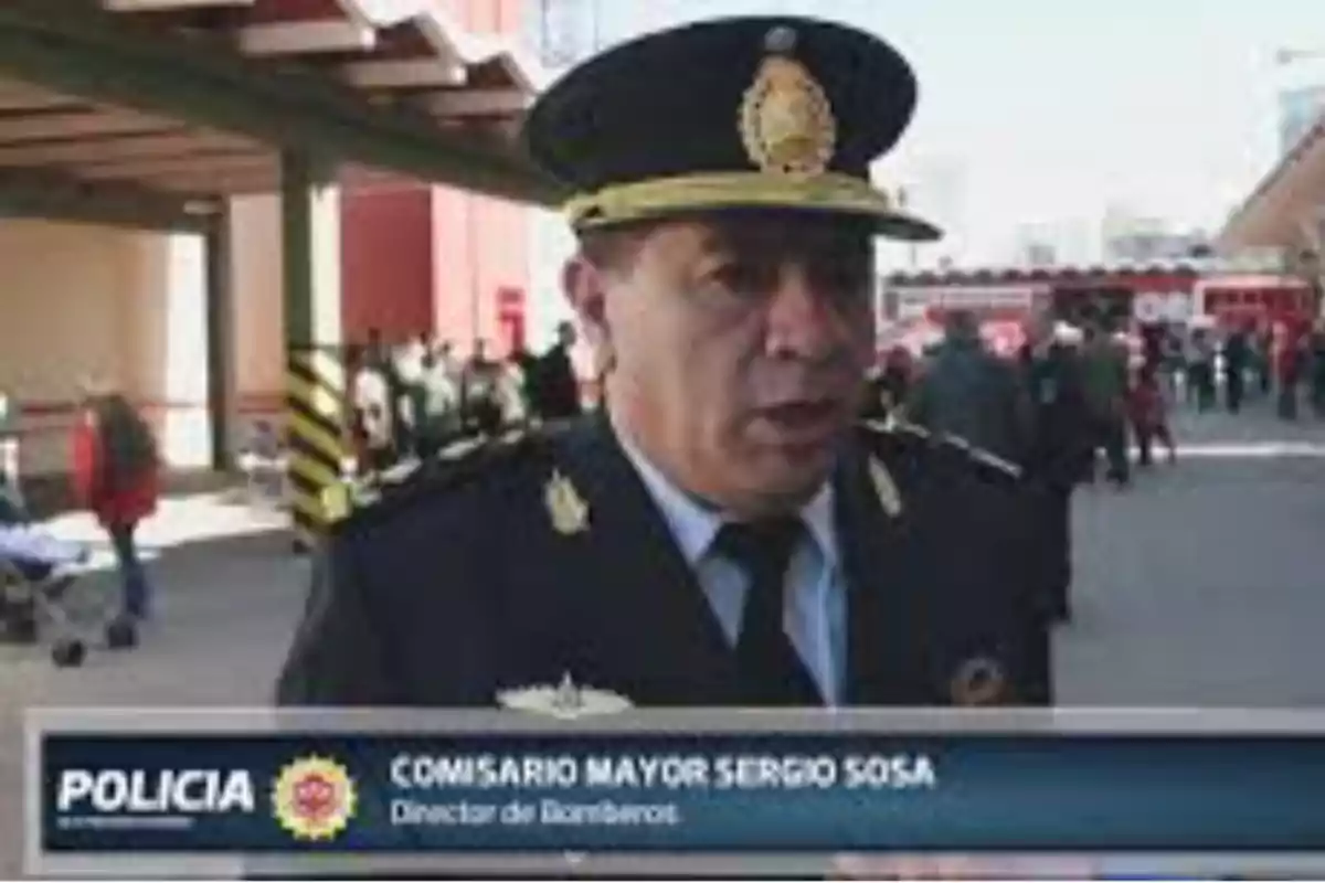 Un comisario mayor de la policía con uniforme y gorra está dando una entrevista en un espacio exterior con personas y un camión de bomberos al fondo Un comisario mayor de la policía con uniforme y gorra está dando una entrevista en un espacio exterior con personas y un camión de bomberos al fondo