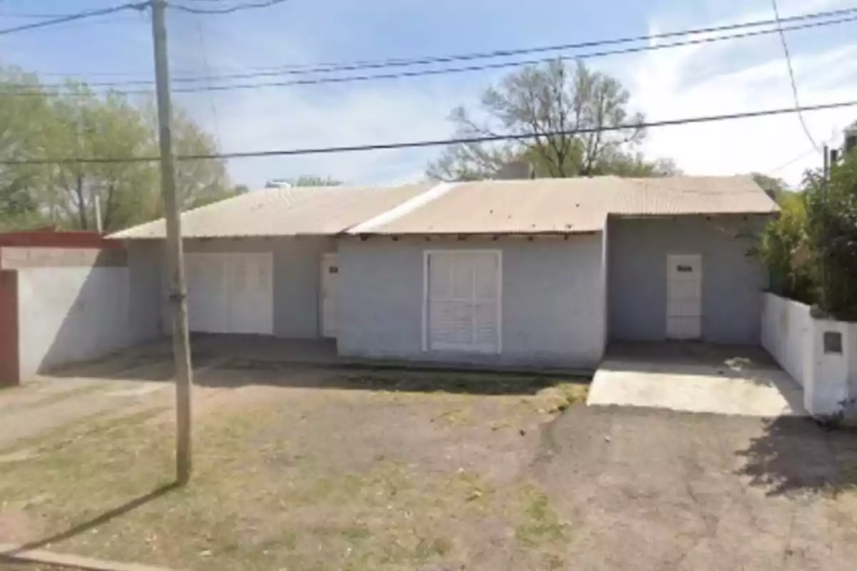 Single-story house with gray walls, metal roof, and several doors and windows at the front, located on a street with grass and a light pole on the sidewalk.