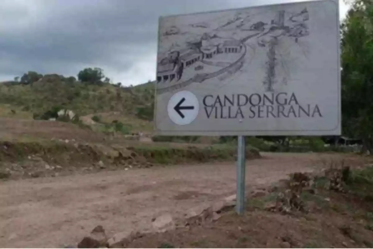Cartel en un camino de tierra señalando hacia la izquierda con el texto Candonga Villa Serrana y un dibujo de edificaciones rurales Cartel en un camino de tierra señalando hacia la izquierda con el texto Candonga Villa Serrana y un dibujo de edificaciones rurales