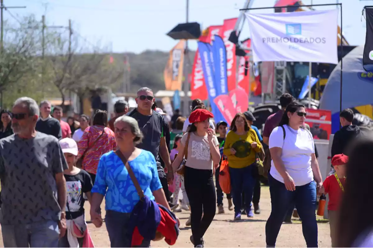 People walking through an outdoor fair on a sunny day with flags and signs in the background People walking through an outdoor fair on a sunny day with flags and signs in the background