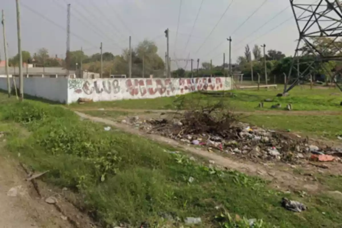 Land with grass and trash in the foreground, in the background a white wall with graffiti and electric poles Land with grass and trash in the foreground, in the background a white wall with graffiti and electric poles