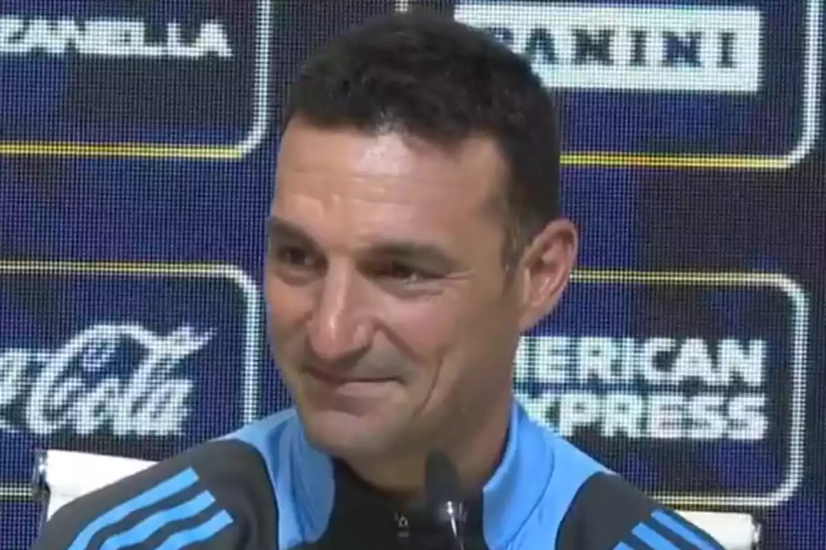 Man in a blue sports jacket smiling during a press conference with brand logos in the background