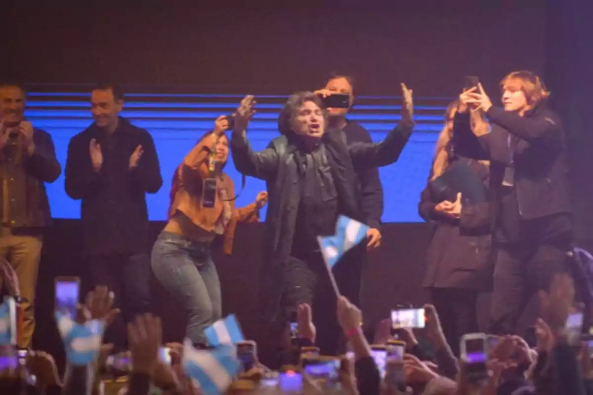 Un grupo de personas celebra en un escenario mientras una multitud levanta banderas argentinas y teléfonos móviles Un grupo de personas celebra en un escenario mientras una multitud levanta banderas argentinas y teléfonos móviles