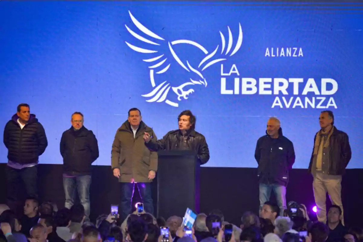 A group of men on a stage during a political event with a blue background displaying an eagle logo and the text A group of men on a stage during a political event with a blue background displaying an eagle logo and the text