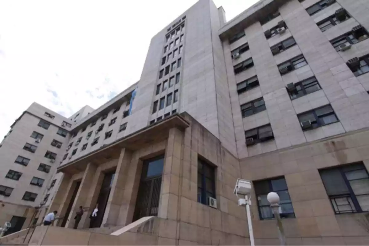 Multi-story government building with a stone facade, rectangular windows, and people entering through the main door Multi-story government building with a stone facade, rectangular windows, and people entering through the main door