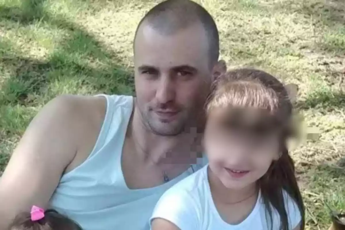 Man in a white tank top sitting on the grass next to a girl with a blurred face