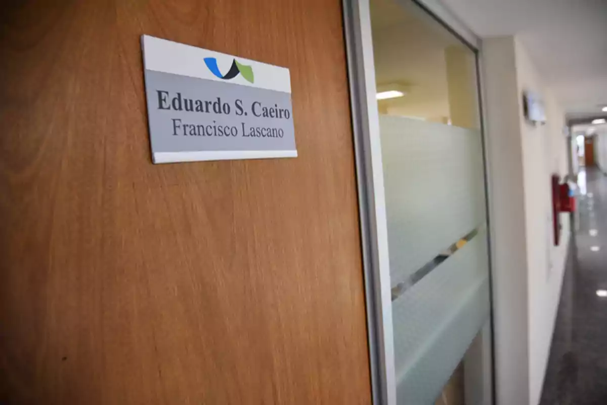 Puerta de oficina de madera con un letrero que tiene los nombres Eduardo S. Caeiro y Francisco Lascano en un pasillo iluminado Puerta de oficina de madera con un letrero que tiene los nombres Eduardo S. Caeiro y Francisco Lascano en un pasillo iluminado