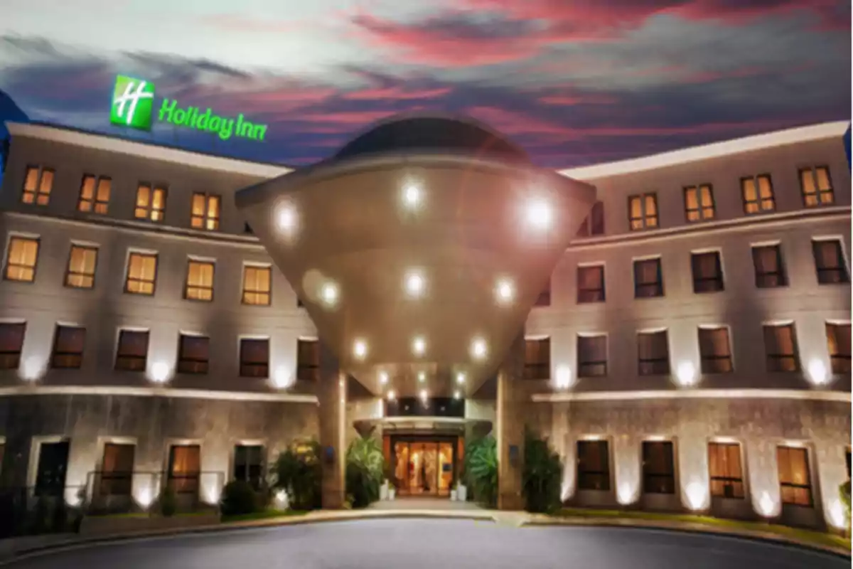Facade of a Holiday Inn hotel with a flying saucer-shaped structure illuminated at the entrance at sunset