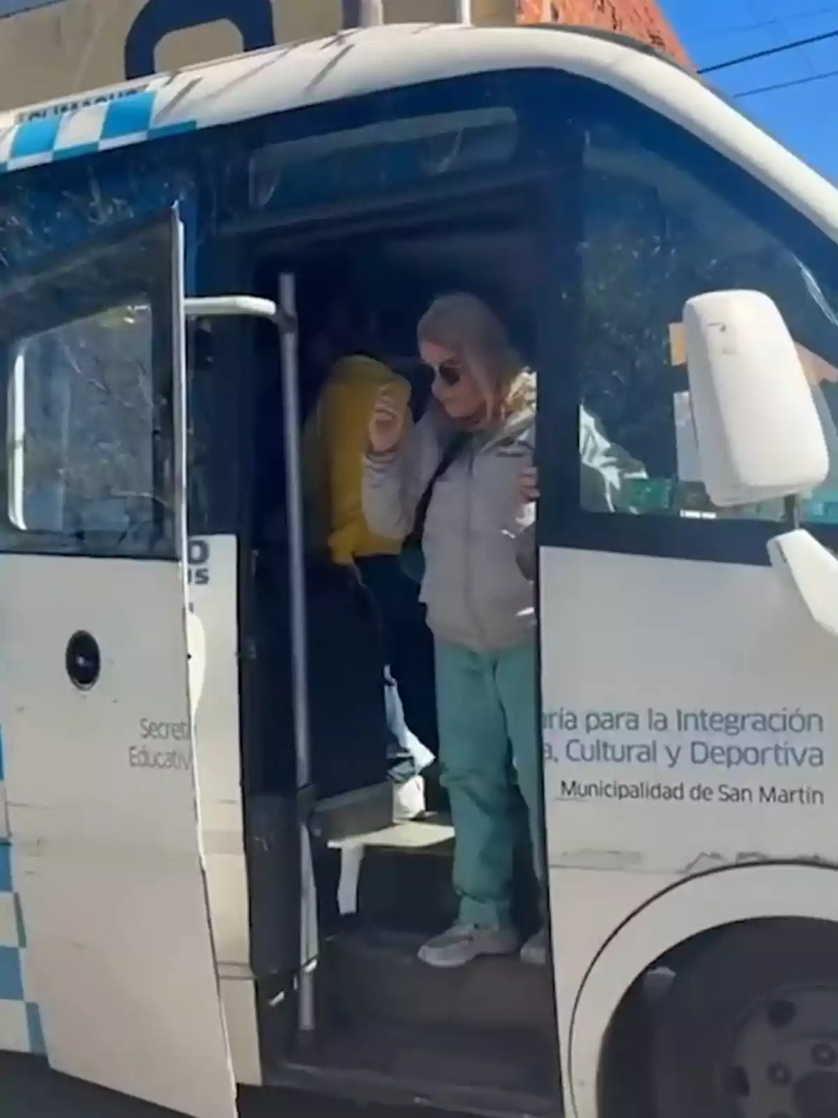 Mujer rubia con gafas de sol bajando de una combi blanca con puertas abiertas y letras en el costado Mujer rubia con gafas de sol bajando de una combi blanca con puertas abiertas y letras en el costado