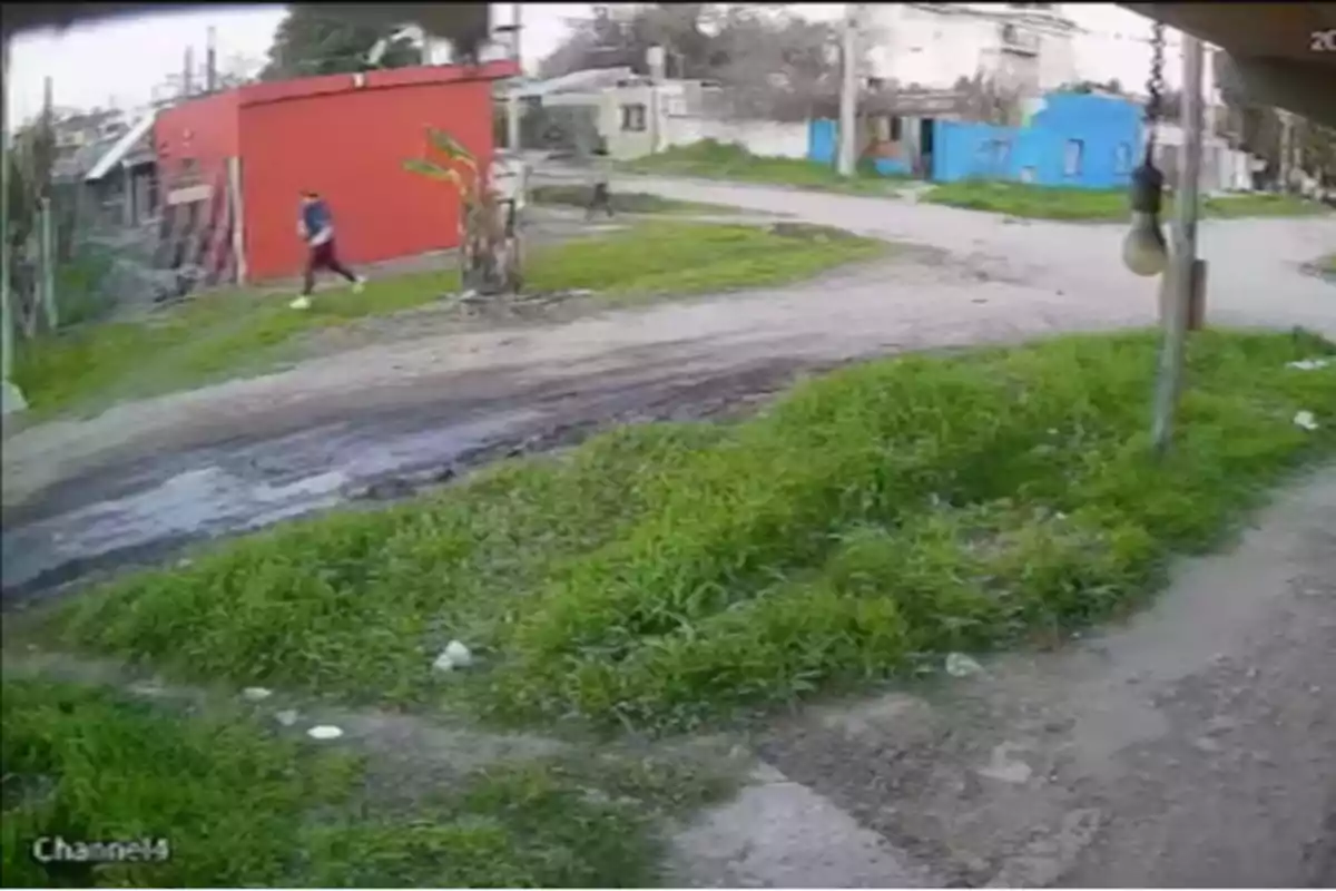 Una persona camina por una calle de tierra en un barrio con casas de colores y vegetación alrededor Una persona camina por una calle de tierra en un barrio con casas de colores y vegetación alrededor