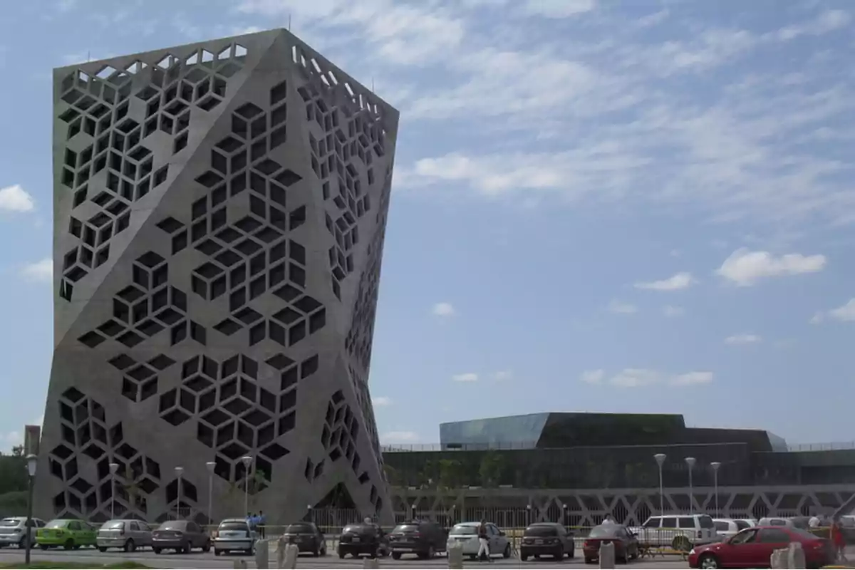 Modern building with a geometric-patterned facade and cars parked in front under a partly cloudy sky